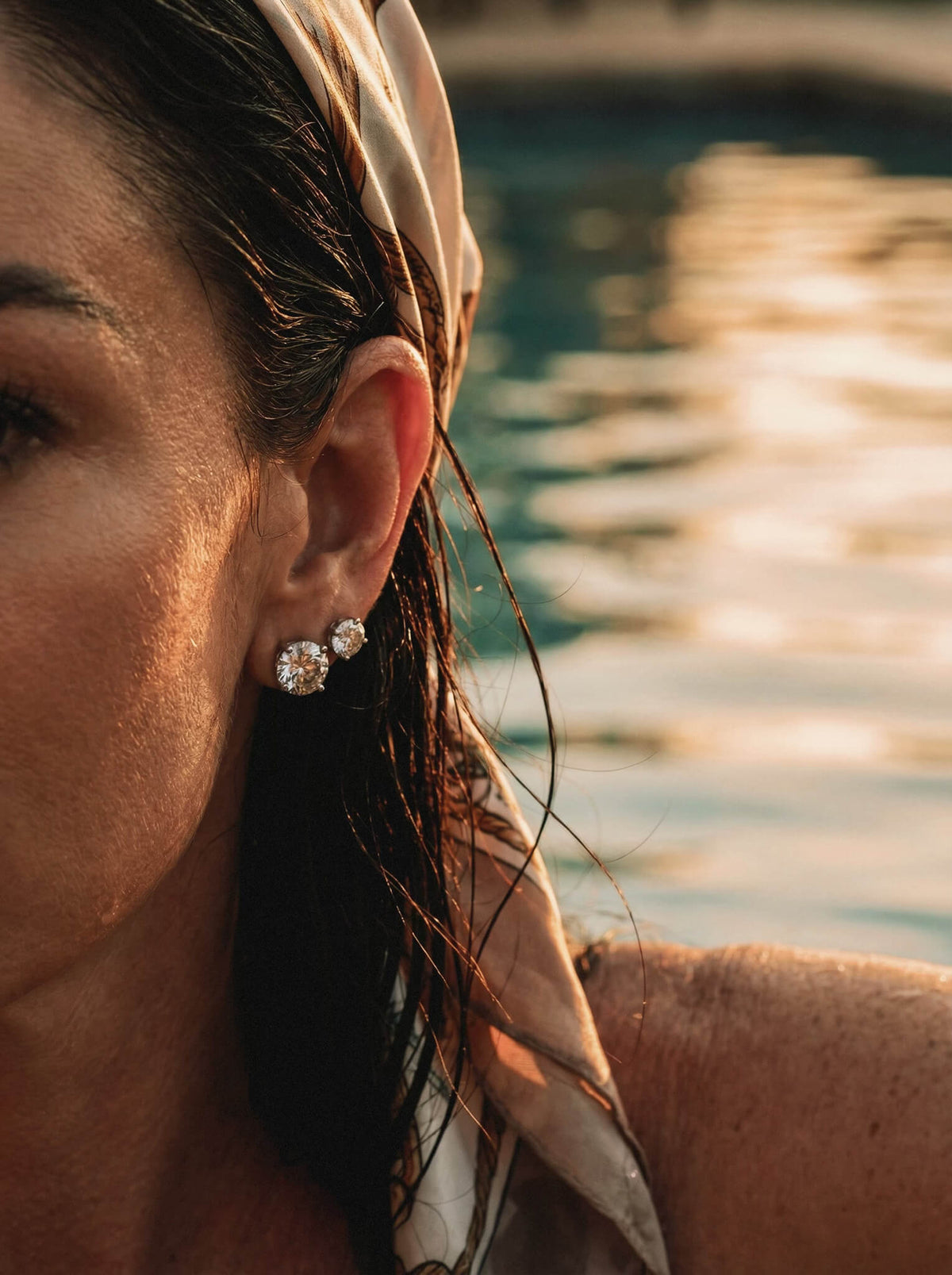 A woman's ear with 2 large diamond earrings in. 