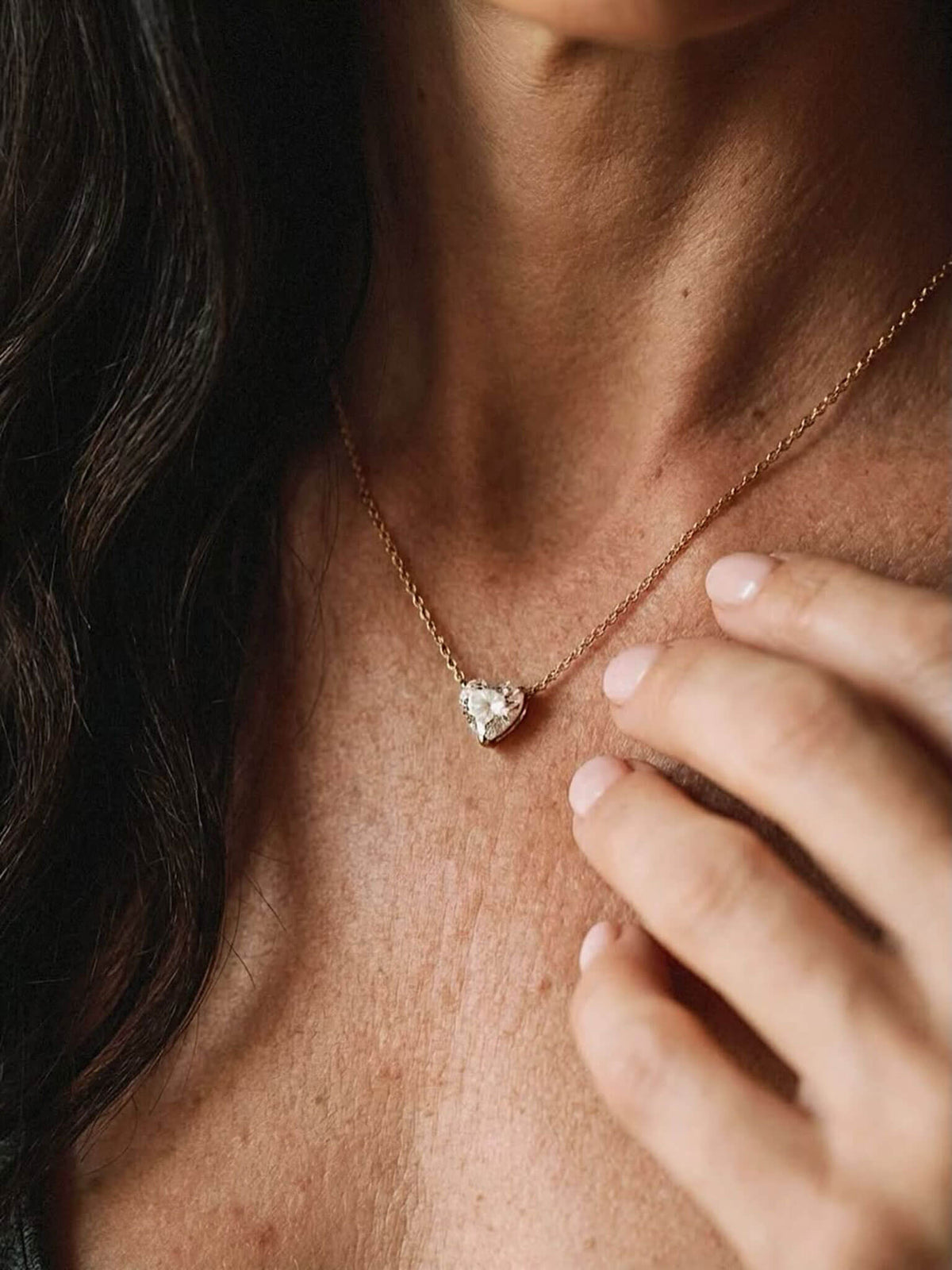 Heart shaped diamond necklace around a woman's neck.