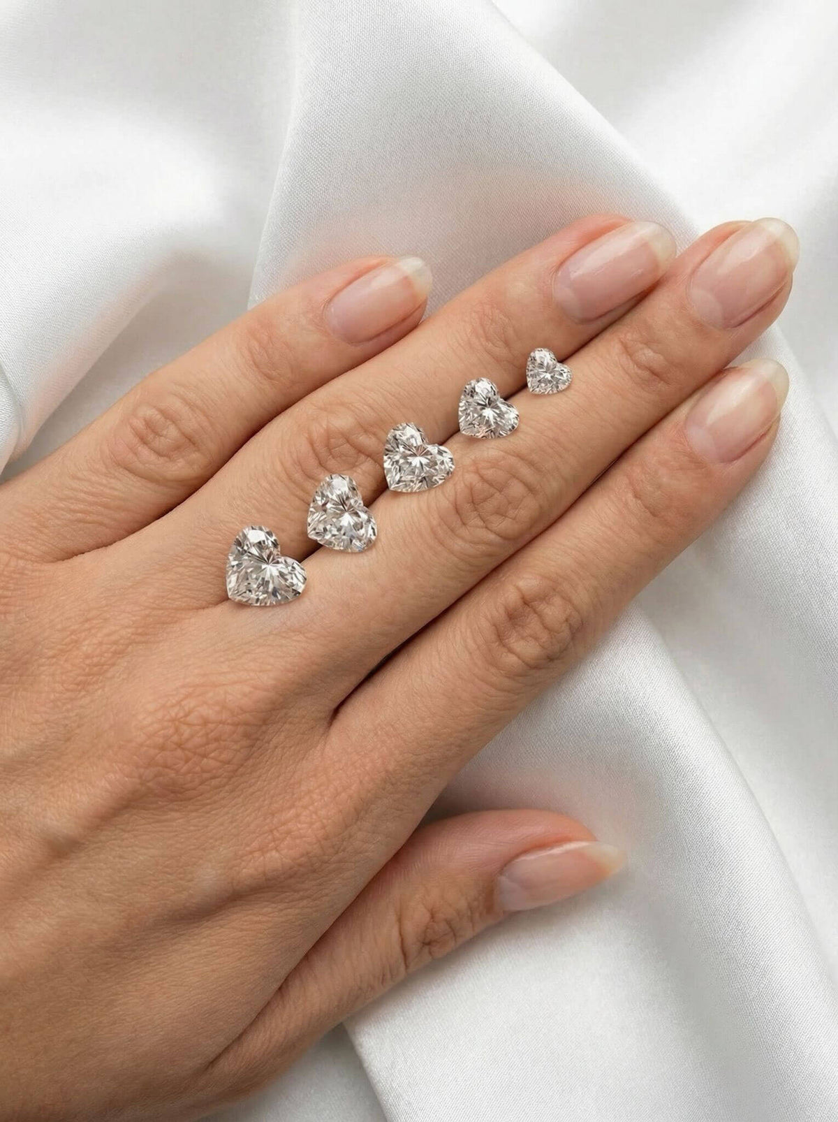5 heart shaped diamonds, in 1-5ct, resting on a woman's hand for scale.